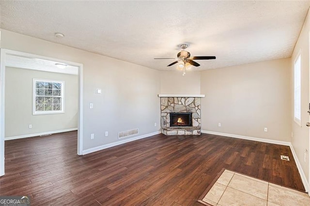 unfurnished living room with a stone fireplace, dark wood-type flooring, a textured ceiling, and ceiling fan