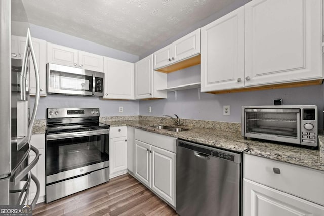 kitchen with sink, white cabinetry, stainless steel appliances, dark hardwood / wood-style floors, and light stone countertops