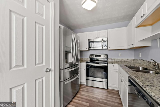 kitchen with sink, white cabinetry, stainless steel appliances, light stone counters, and dark hardwood / wood-style flooring