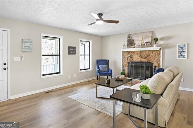 living room with ceiling fan, a fireplace, light hardwood / wood-style floors, and a textured ceiling