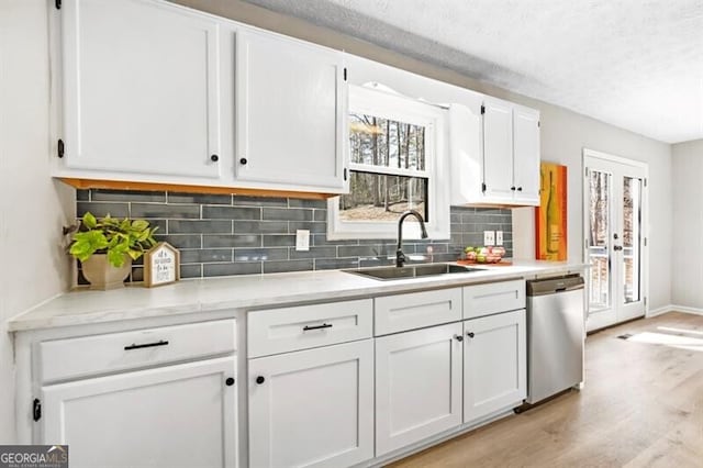 kitchen featuring sink, white cabinetry, decorative backsplash, stainless steel dishwasher, and light wood-type flooring