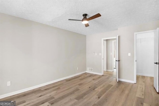 unfurnished bedroom featuring a spacious closet, a textured ceiling, light wood-type flooring, and a closet