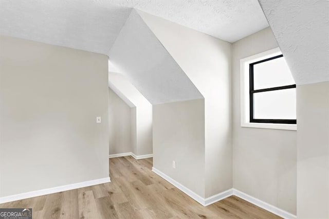 additional living space with lofted ceiling, a textured ceiling, and light wood-type flooring