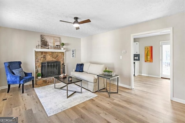 living room with ceiling fan, a stone fireplace, light hardwood / wood-style floors, and a textured ceiling