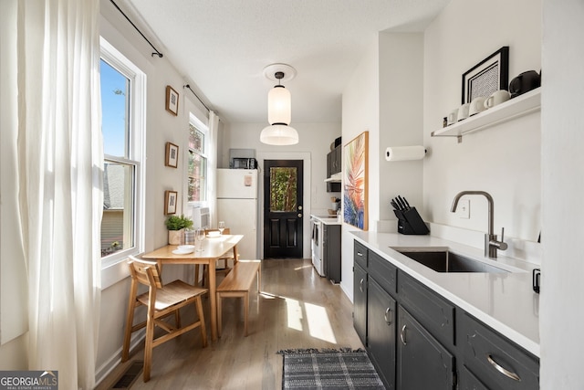 kitchen with decorative light fixtures, separate washer and dryer, sink, dark wood-type flooring, and white appliances