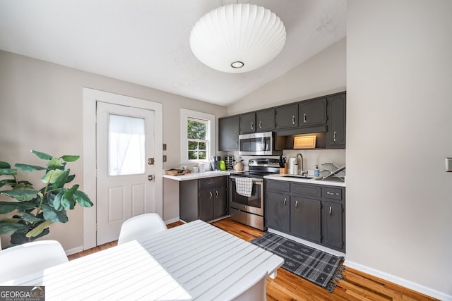 kitchen featuring lofted ceiling, appliances with stainless steel finishes, sink, and light wood-type flooring