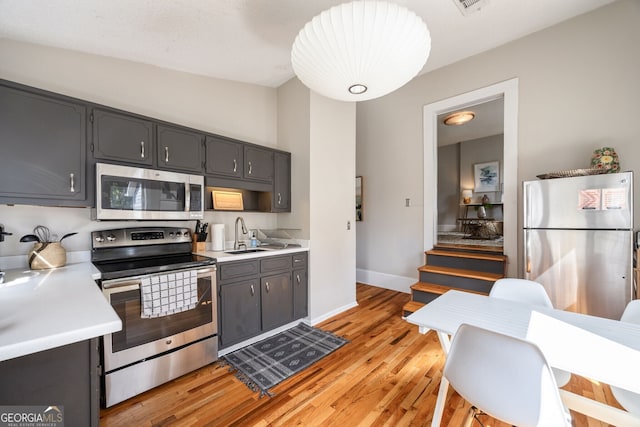 kitchen with appliances with stainless steel finishes, sink, and light hardwood / wood-style flooring