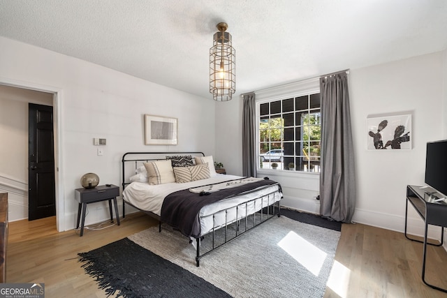 bedroom with an inviting chandelier, light hardwood / wood-style flooring, and a textured ceiling