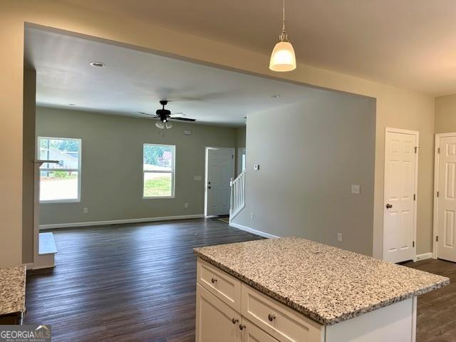 kitchen featuring light stone counters, hanging light fixtures, dark hardwood / wood-style floors, ceiling fan, and white cabinets