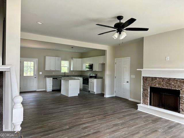 unfurnished living room featuring sink, a stone fireplace, dark wood-type flooring, and ceiling fan