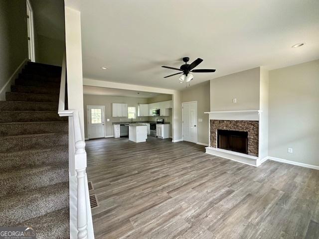 unfurnished living room with hardwood / wood-style flooring, a stone fireplace, and ceiling fan