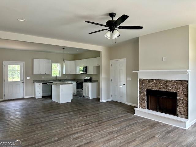 kitchen with a stone fireplace, white cabinetry, a center island, stainless steel appliances, and dark wood-type flooring