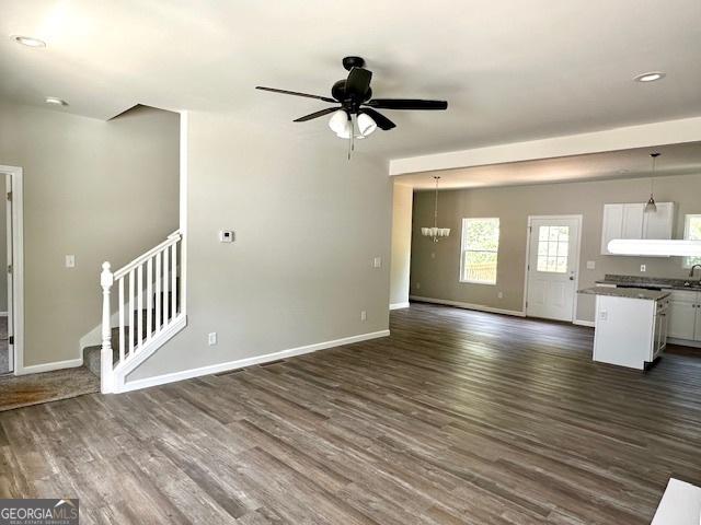 unfurnished living room featuring dark hardwood / wood-style floors and ceiling fan with notable chandelier