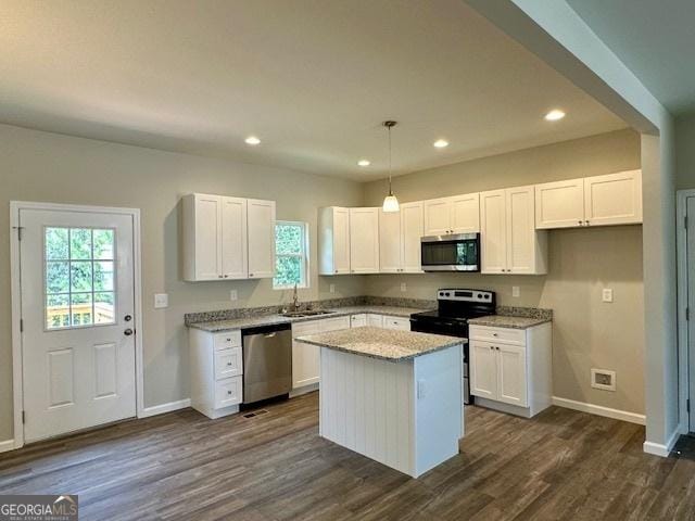 kitchen with appliances with stainless steel finishes, light stone counters, white cabinets, a kitchen island, and decorative light fixtures