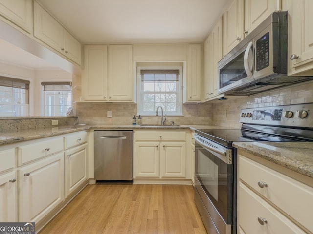 kitchen with sink, backsplash, stainless steel appliances, light stone counters, and light hardwood / wood-style floors