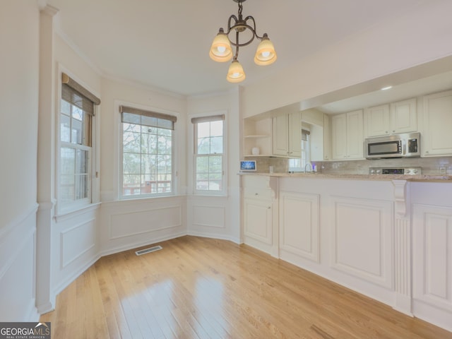 kitchen with tasteful backsplash, white cabinets, light hardwood / wood-style floors, and decorative light fixtures