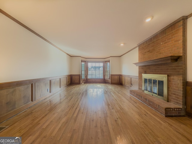 unfurnished living room featuring crown molding, a brick fireplace, and light wood-type flooring