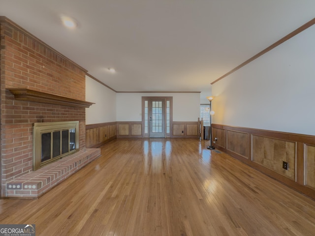 unfurnished living room with ornamental molding, a fireplace, light hardwood / wood-style floors, and french doors