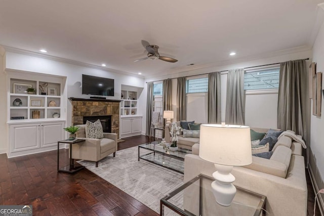 living room featuring built in features, ceiling fan, a fireplace, ornamental molding, and dark hardwood / wood-style flooring