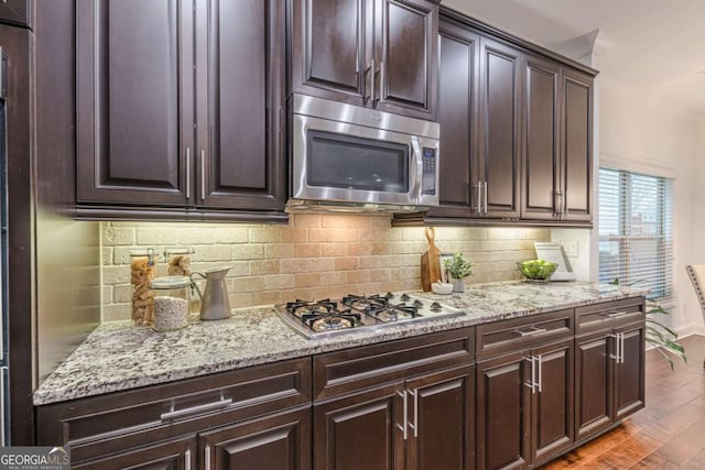 kitchen with stainless steel appliances, wood-type flooring, dark brown cabinets, and backsplash