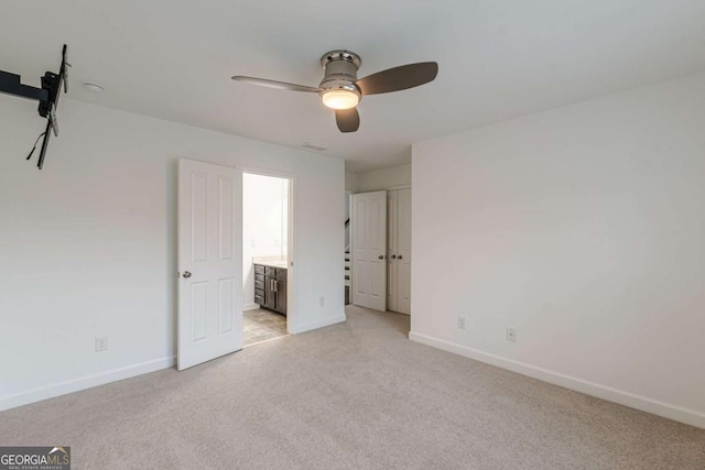 unfurnished bedroom with ceiling fan, ensuite bathroom, and light carpet