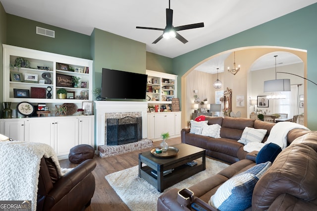 living room featuring wood-type flooring, ceiling fan with notable chandelier, and a brick fireplace