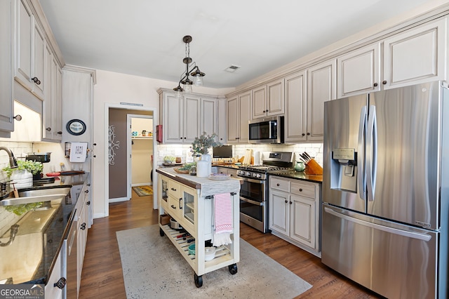 kitchen featuring sink, decorative backsplash, hanging light fixtures, stainless steel appliances, and dark wood-type flooring