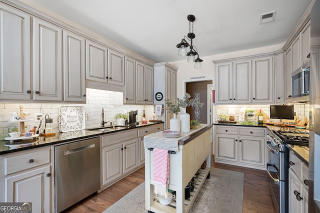 kitchen featuring sink, appliances with stainless steel finishes, hanging light fixtures, dark hardwood / wood-style flooring, and dark stone counters