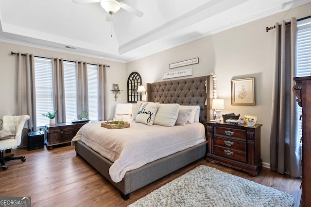 bedroom with a raised ceiling, ornamental molding, dark wood-type flooring, and ceiling fan