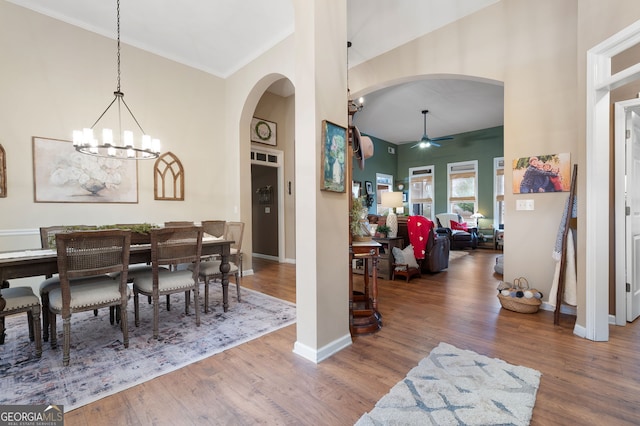 dining area with crown molding, ceiling fan with notable chandelier, a towering ceiling, and hardwood / wood-style floors