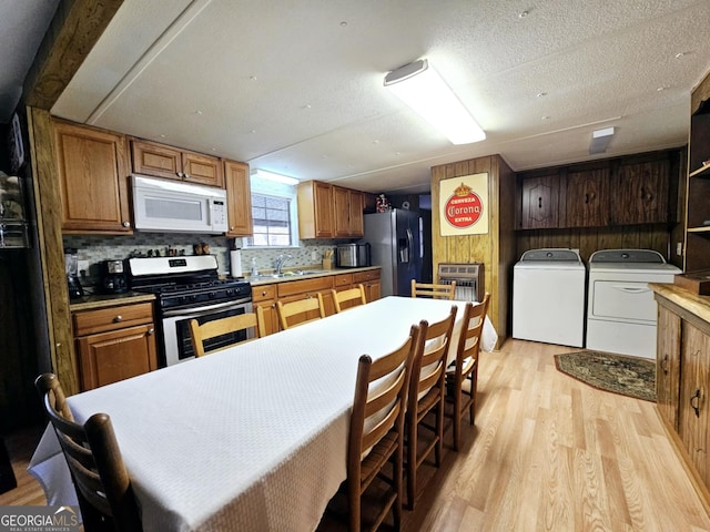 kitchen with light hardwood / wood-style flooring, appliances with stainless steel finishes, tasteful backsplash, washing machine and clothes dryer, and wood walls