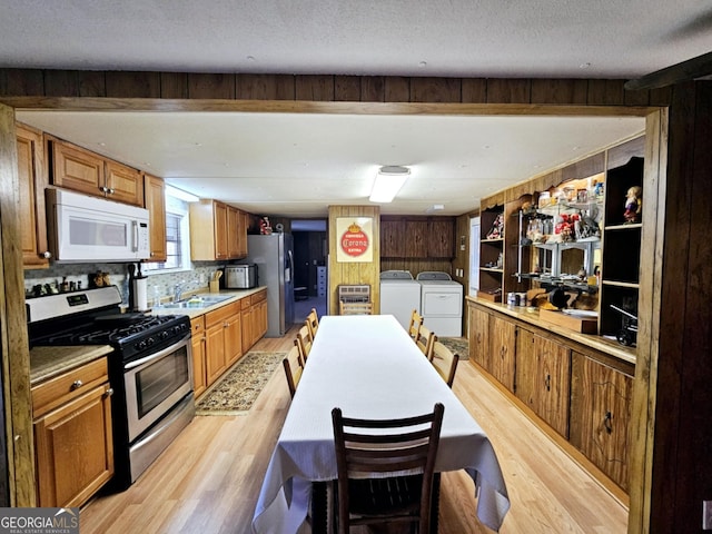 kitchen with washing machine and clothes dryer, sink, light hardwood / wood-style flooring, a textured ceiling, and stainless steel appliances