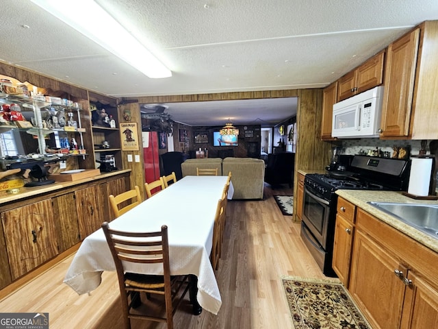 kitchen featuring wood walls, gas range oven, a textured ceiling, and light wood-type flooring