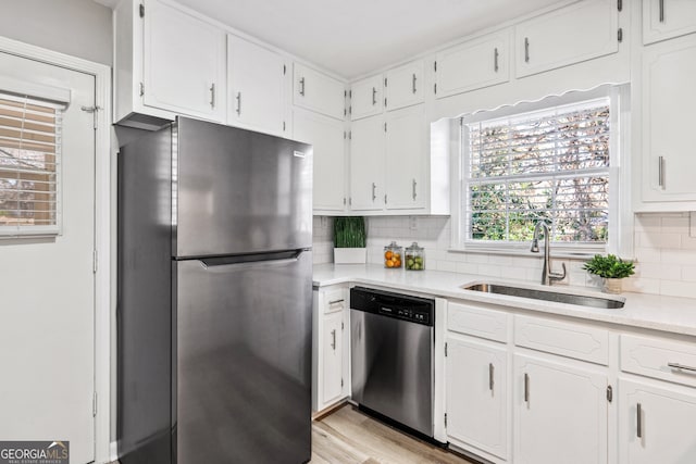 kitchen with sink, light hardwood / wood-style flooring, appliances with stainless steel finishes, white cabinets, and decorative backsplash