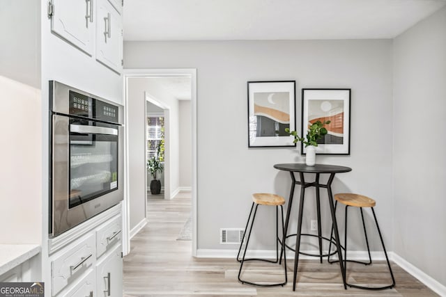 kitchen featuring white cabinetry, light hardwood / wood-style flooring, a kitchen breakfast bar, and stainless steel oven