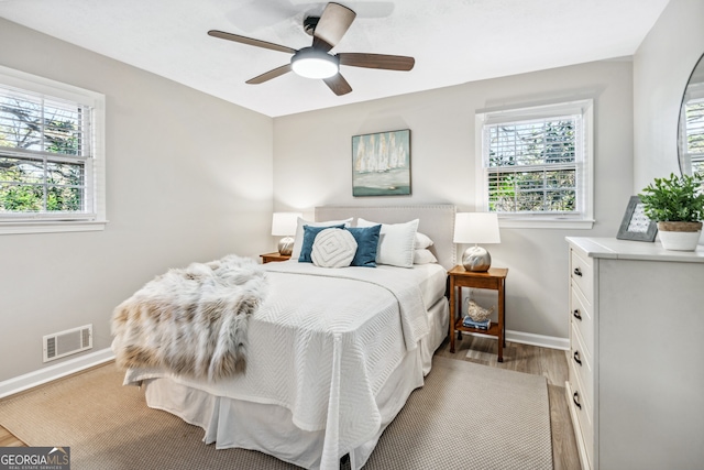 bedroom with ceiling fan, multiple windows, and light hardwood / wood-style flooring