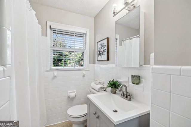 bathroom with vanity, toilet, a textured ceiling, and tile walls