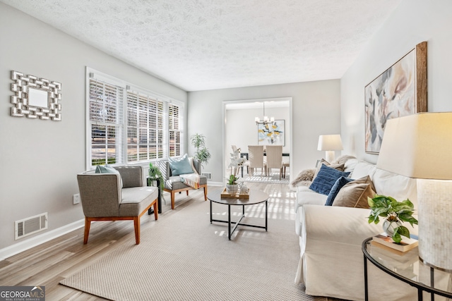 living room with a textured ceiling, an inviting chandelier, and light hardwood / wood-style flooring