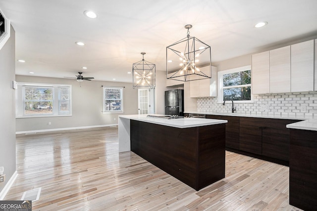 kitchen featuring a kitchen bar, black fridge, hanging light fixtures, a center island with sink, and backsplash