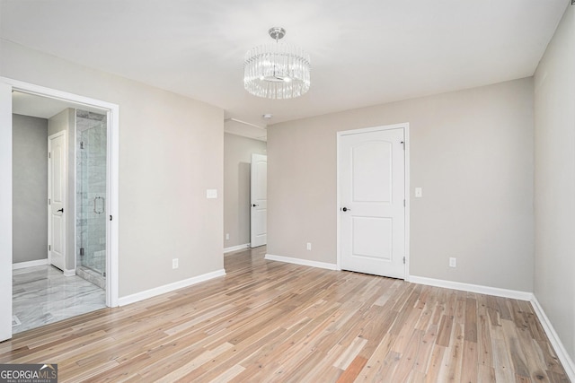 unfurnished bedroom with ensuite bath, a chandelier, and light hardwood / wood-style flooring