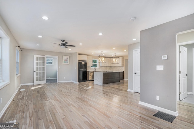 unfurnished living room featuring ceiling fan with notable chandelier and light wood-type flooring