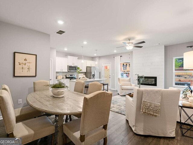 dining room featuring a large fireplace, dark hardwood / wood-style floors, and ceiling fan