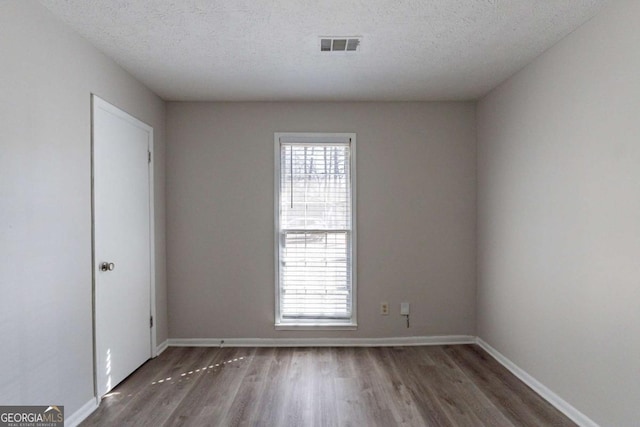 empty room featuring plenty of natural light, dark hardwood / wood-style floors, and a textured ceiling