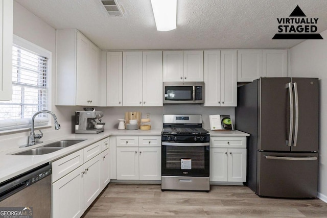 kitchen with sink, light wood-type flooring, white cabinets, and appliances with stainless steel finishes