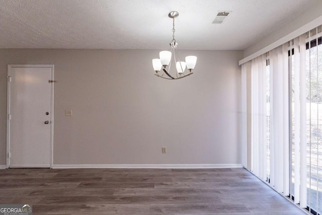 spare room with dark hardwood / wood-style floors, a textured ceiling, and a notable chandelier
