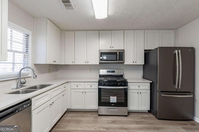 kitchen featuring white cabinetry, stainless steel appliances, sink, and light hardwood / wood-style flooring