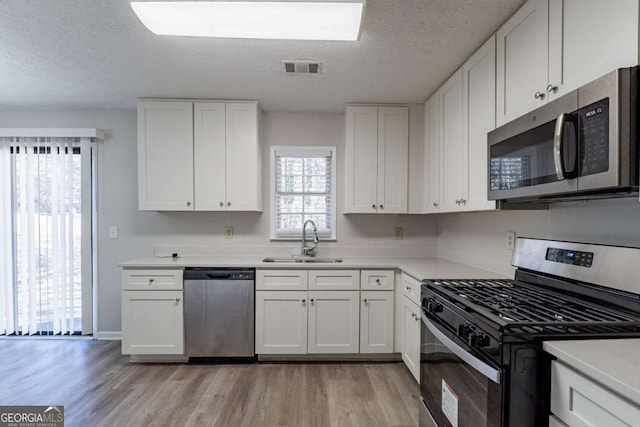 kitchen with white cabinetry, sink, stainless steel appliances, and light wood-type flooring