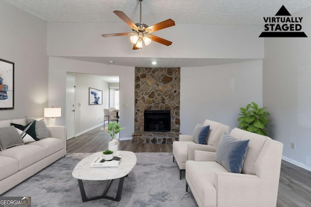 living room with wood-type flooring, a stone fireplace, and a textured ceiling