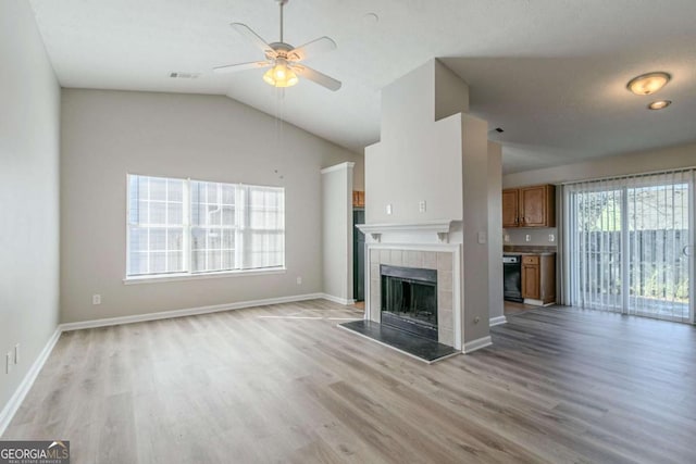 unfurnished living room with ceiling fan, lofted ceiling, a tiled fireplace, and light hardwood / wood-style flooring