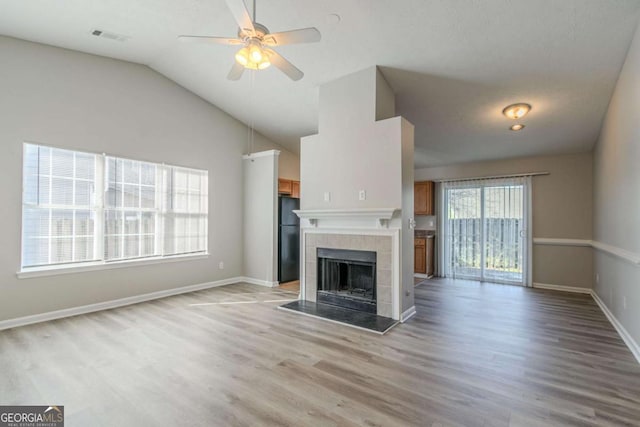 unfurnished living room featuring vaulted ceiling, ceiling fan, light hardwood / wood-style floors, and a tile fireplace